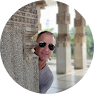 A man with sunglasses is smiling behind some pillars.