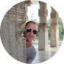 A man with sunglasses is smiling behind some pillars.